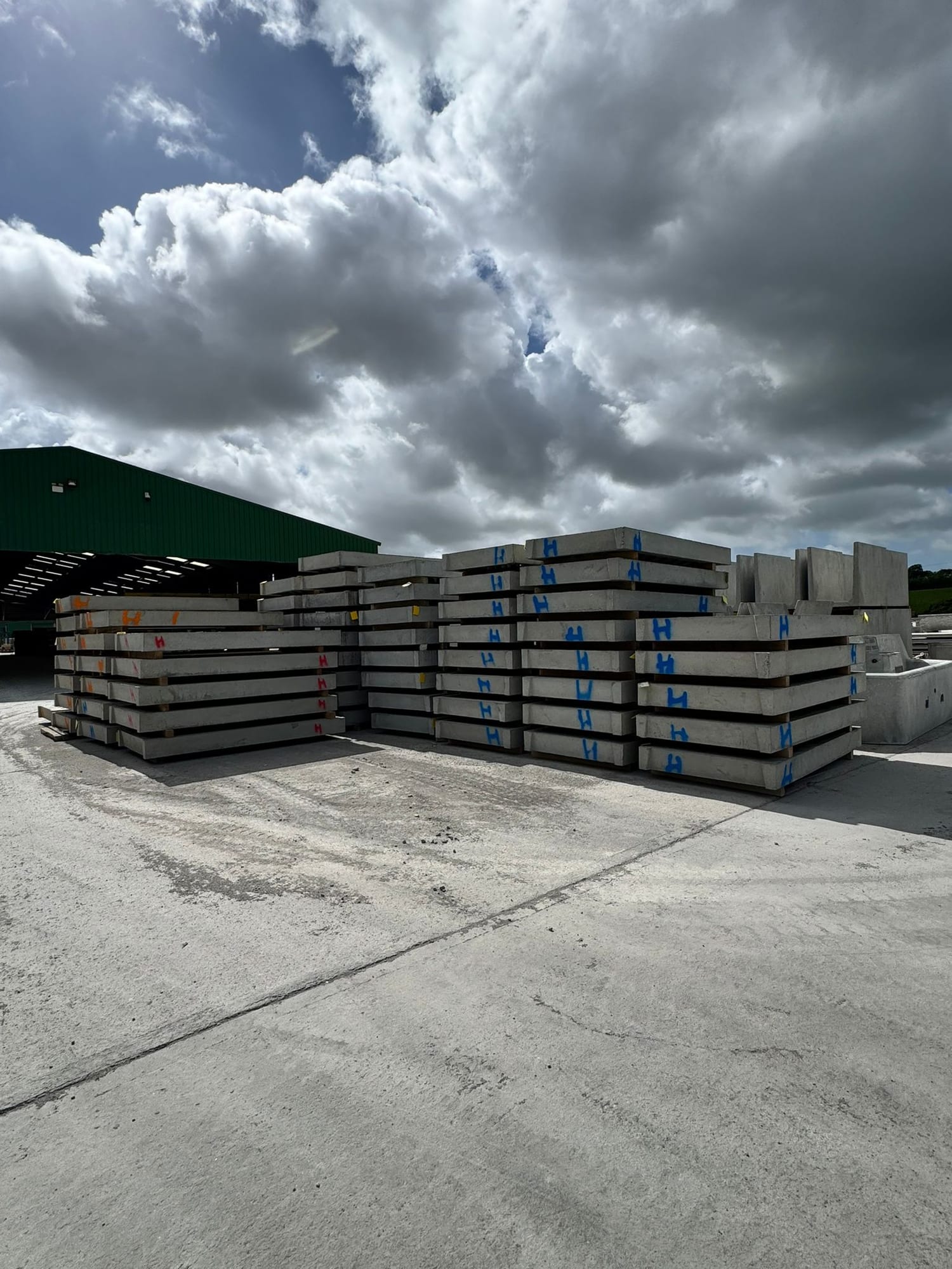 Prestressed concrete wall panels stacked flat on timber bearers with colour-coded height markings at the WCCP yard, Chilsworthy, Devon, factory building behind