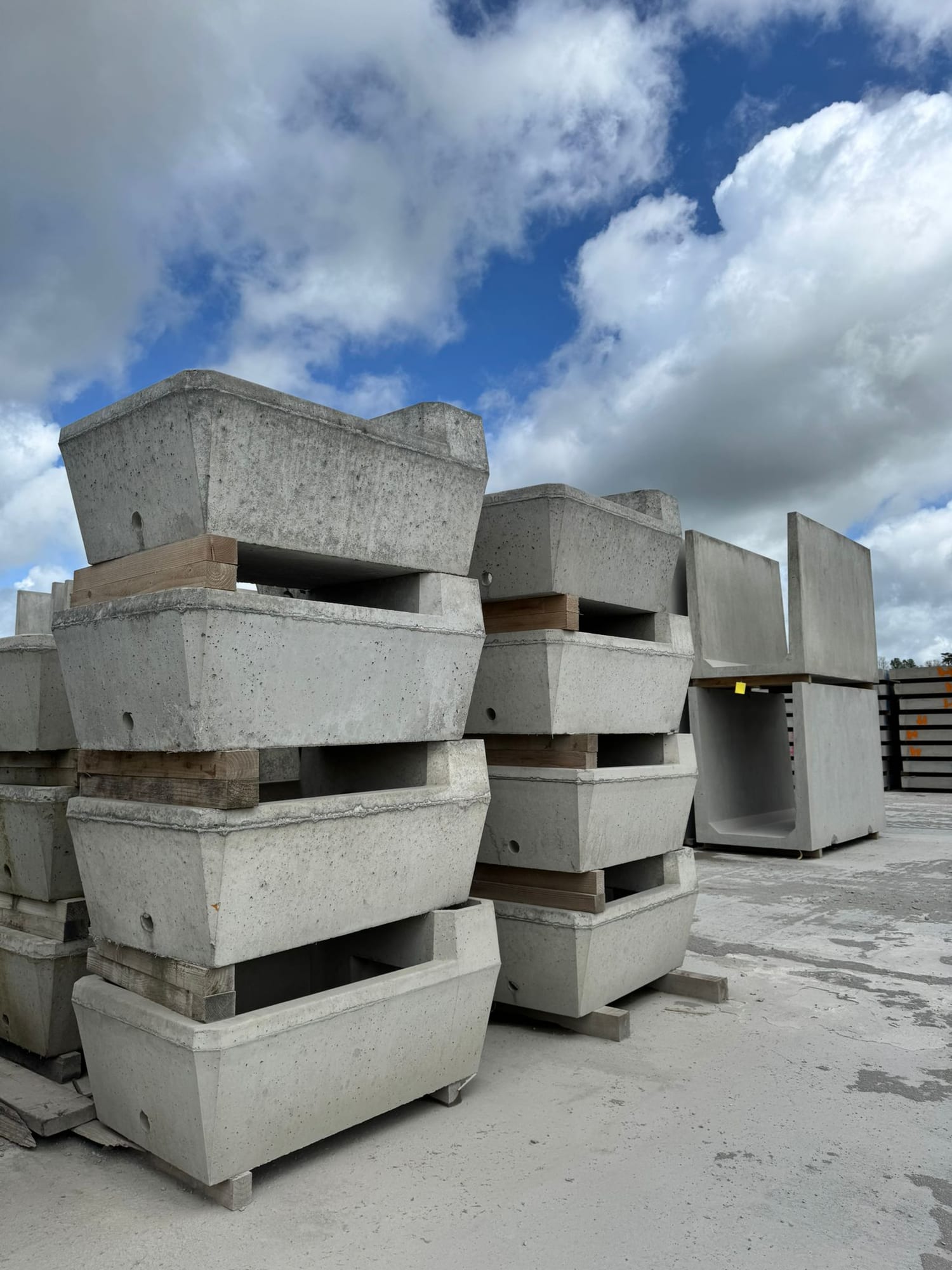 Precast concrete trapezoid headwall units with lifting holes stacked three-high at WCCP Devon, showing tapered profile detail