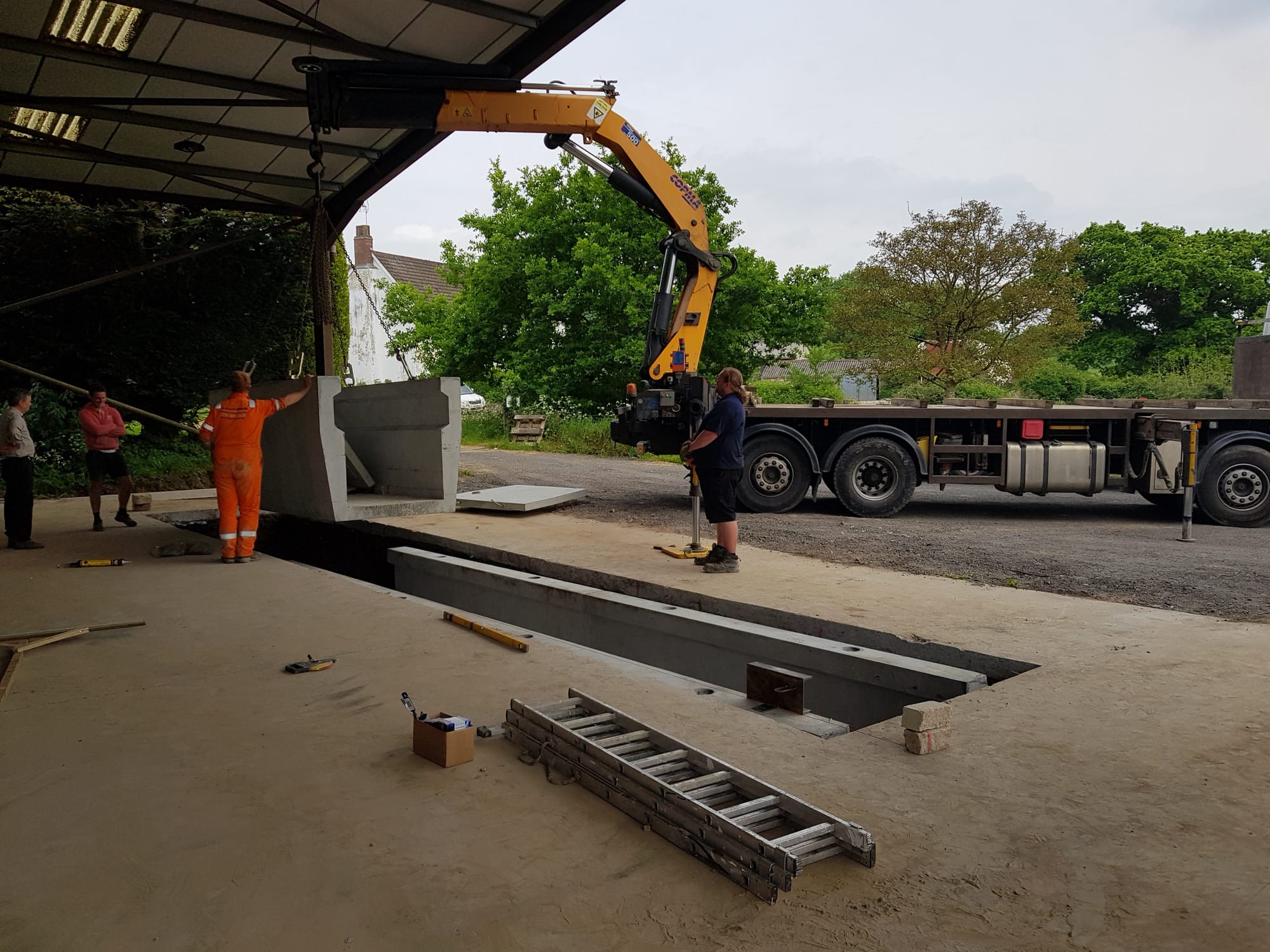 Lorry-mounted crane lifting a WCCP precast concrete inspection-pit section into a prepared excavation, Devon