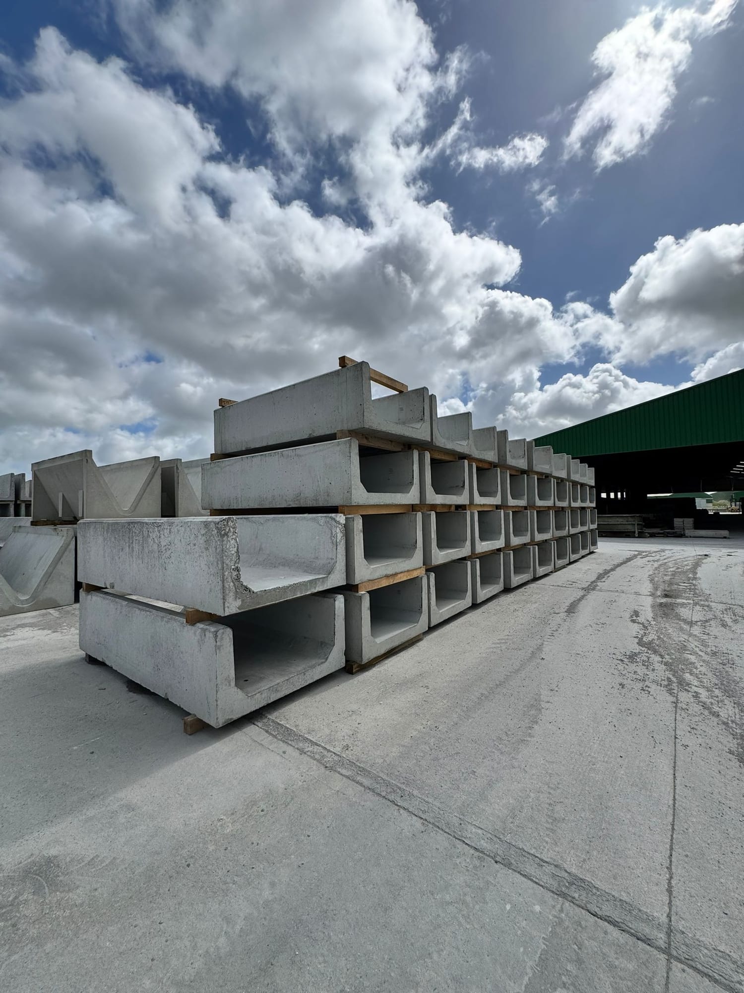 Mixed sizes of precast concrete slurry channels and V-troughs stacked in the WCCP yard with factory building behind, Chilsworthy, Devon