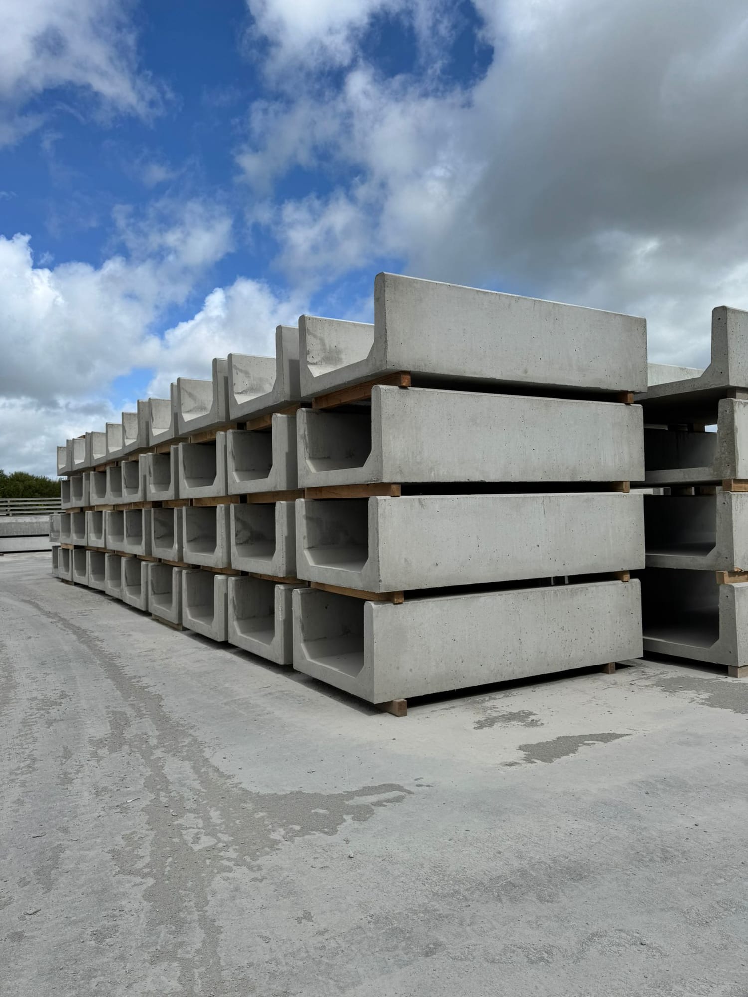 Precast concrete U-profile slurry channels stacked four tiers high on timber bearers at WCCP Devon, showing clean internal profile