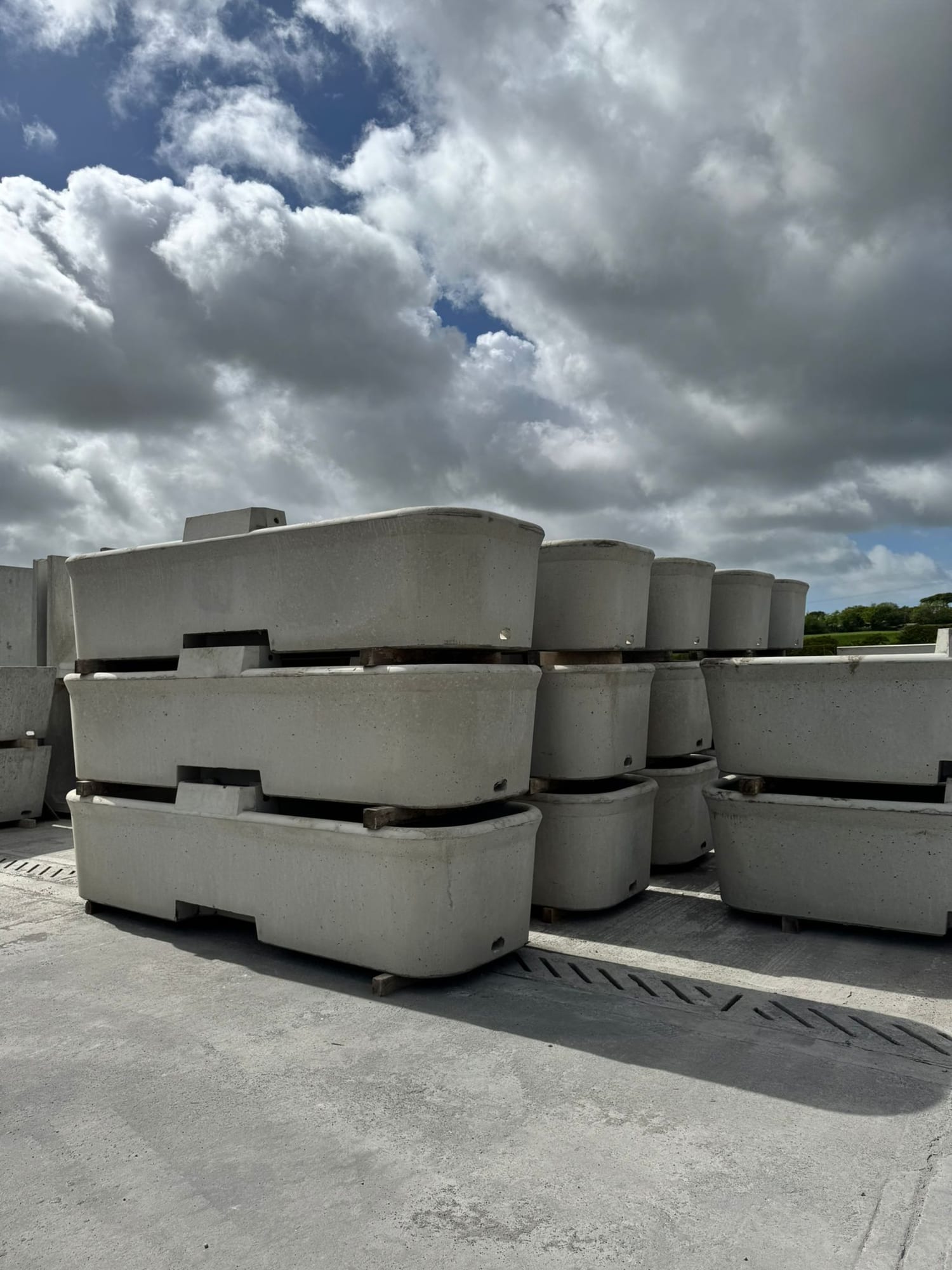Rows of precast concrete cattle drinking troughs with rounded ends stacked on pallets in the WCCP yard at Chilsworthy, Devon
